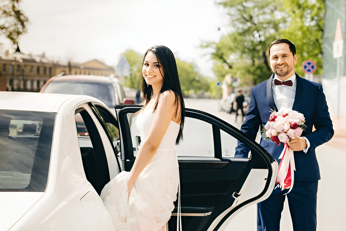 Gelin arabaya binerken damat elinde çiçekle yanında duruyor.