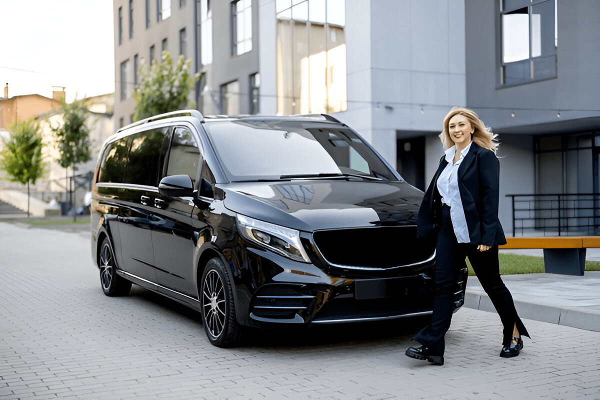 Siyah VIP minibüsün önünde duran profesyonel şoförlü transfer görevlisi kadın